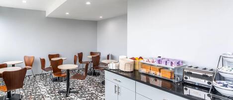 A modern kitchen with a black countertop, white cabinets, and a patterned floor. There are several chairs and tables arranged for dining.