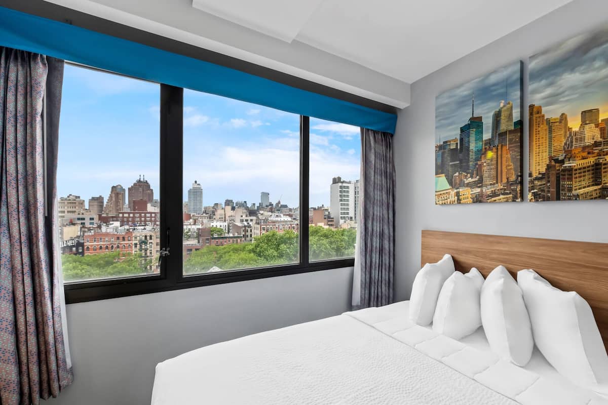 A hotel room with a large bed, a city view, and a painting of the skyline.
