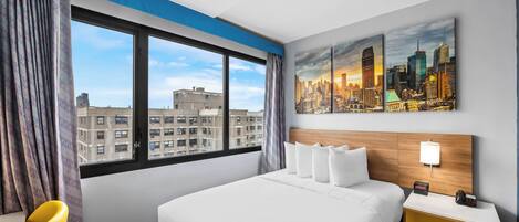 Habitación de hotel con una cama grande, vistas a la ciudad, un escritorio con lámpara y una silla.