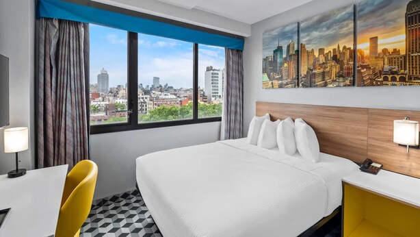 Habitació d'hotel amb un llit gran, una taula de treball, una cadira i vista a la ciutat.