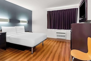 A hotel room with a bed, bedside table, chair, window with curtains, and a wall-mounted TV.