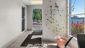Een hotelgang met een potplant, uitzicht naar buiten en een deur naar een parkeerplaats.