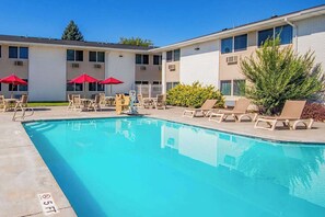 A swimming pool with lounge chairs and umbrellas, a building with multiple windows, and a clear sky. - Econo Lodge Idaho Falls, ID (Idaho Falls)