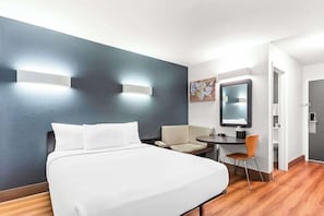 A hotel room with a bed, a desk, a chair, a mirror, and a wall-mounted light fixture. - Econo Lodge Idaho Falls, ID (Idaho Falls)