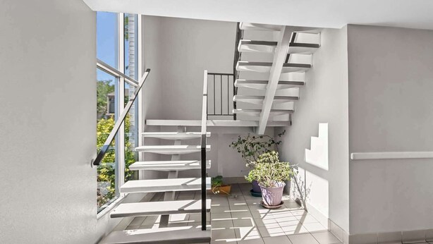 Een modern interieur met een trap, een potplant en uitzicht door een raam.