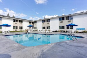 A swimming pool with lounge chairs and umbrellas, surrounded by a building with multiple windows and air conditioning units. - Econo Lodge Idaho Falls, ID (Idaho Falls)