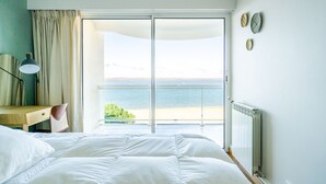 A bedroom with a large bed, a desk, and a view of the sea through a sliding door.