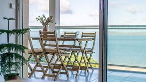 A balcony with a wooden table and chairs, a potted plant, and a view of the sea.