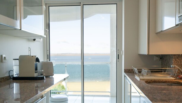 A kitchen with a view of the beach through a sliding glass door.
