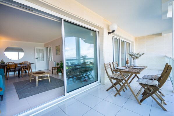 A modern living room with a sliding glass door leading to a balcony, a dining area with wooden furniture, and a view of the outdoors.