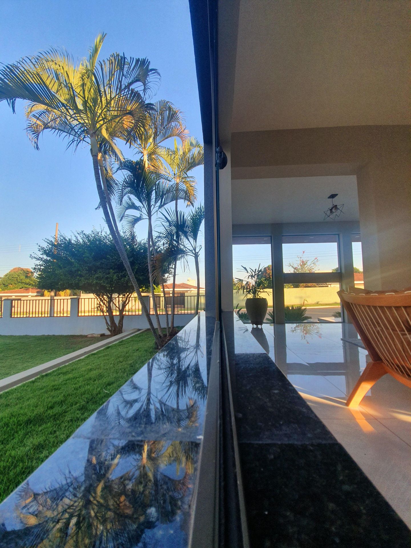 A modern interior with a glass wall reflecting palm trees and a clear sky.