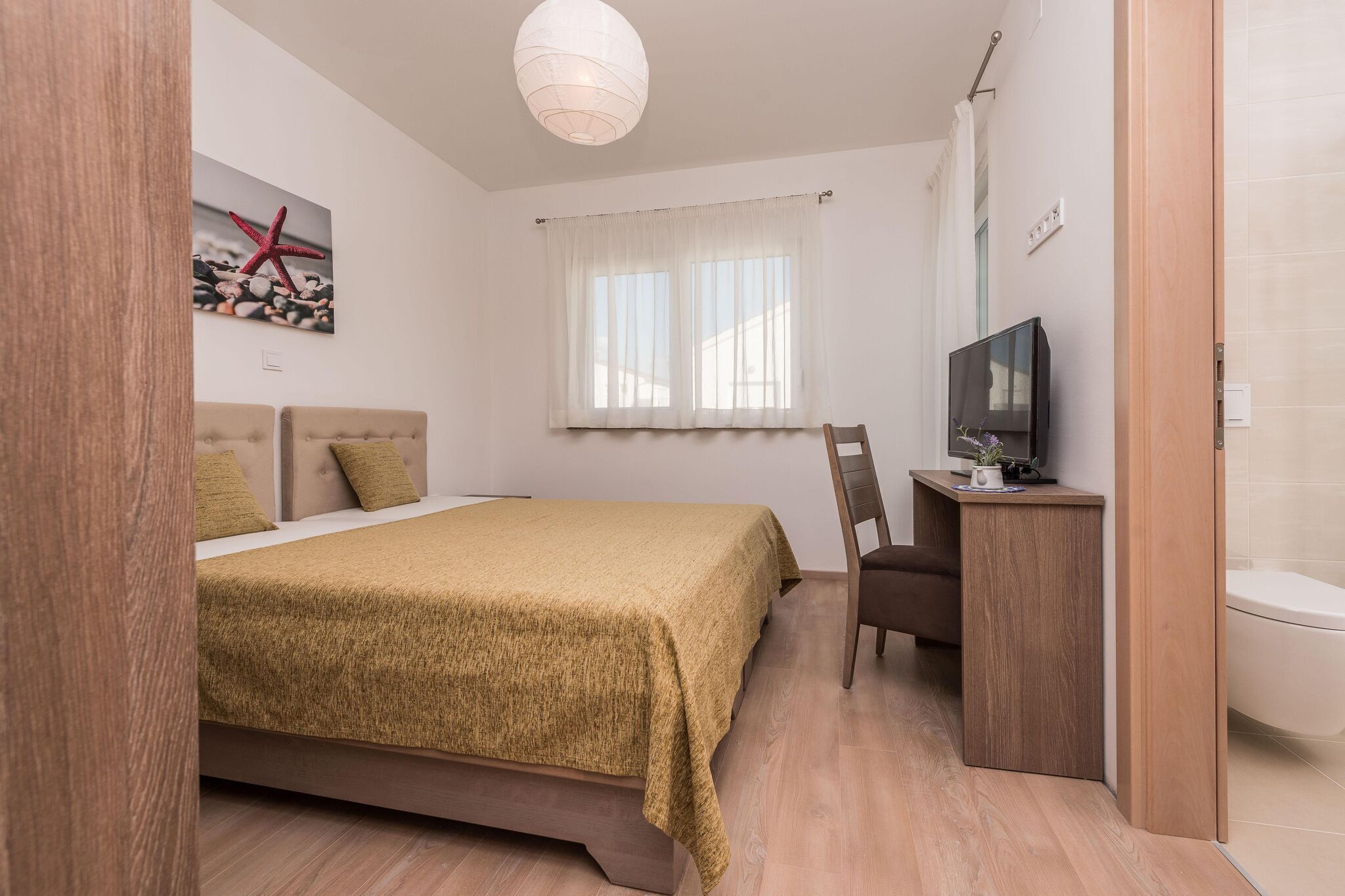 Een slaapkamer met een bed, een televisie, een bureau en een raam met gordijnen.