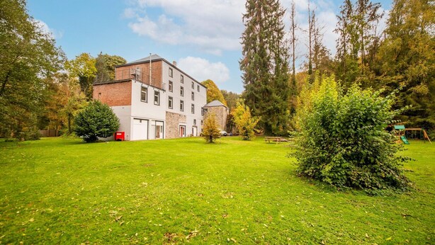 A large building with multiple windows and a brick facade, surrounded by a well-maintained lawn and trees. - Charming Chalet in Falaën by River & Château (Falaën)