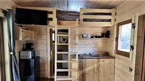 A compact wooden cabin with a kitchenette, a TV mounted above the counter, and a ladder leading to a loft area. - Charming Chalet in Falaën by River & Château (Falaën)