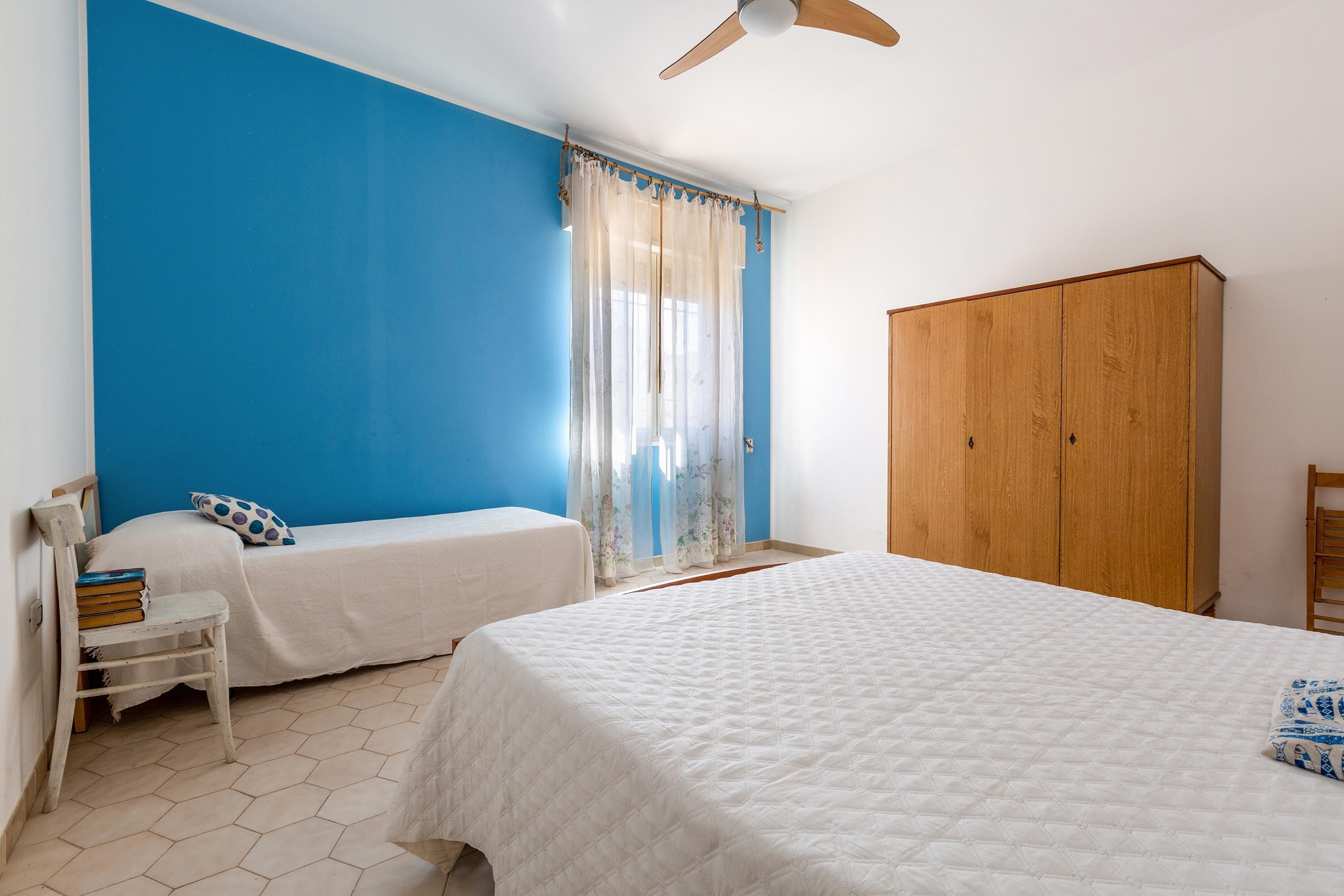 Une chambre avec deux lits, une armoire en bois et une fenêtre ornée de rideaux légers.