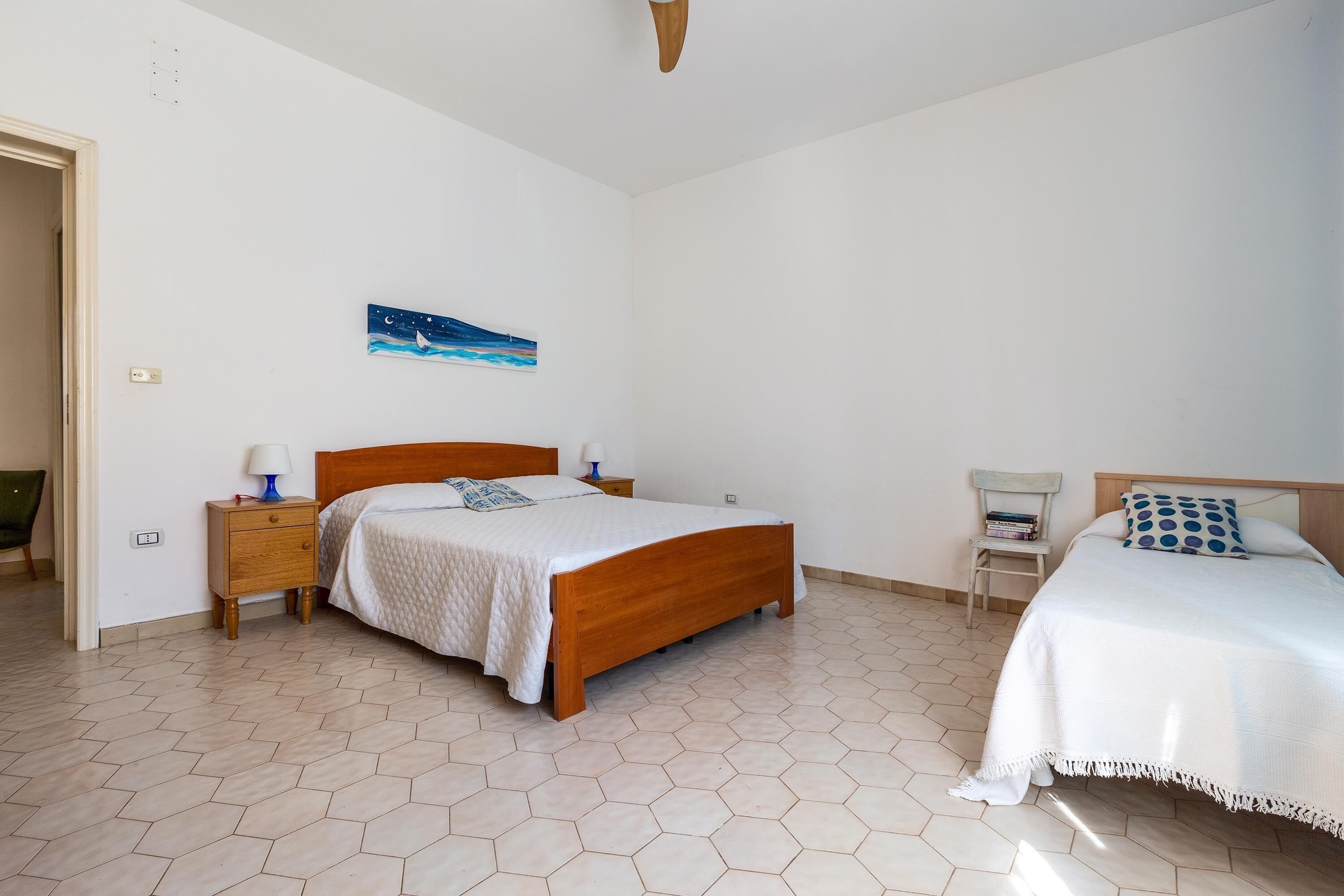Une chambre avec deux lits, une table de chevet, une chaise et un tableau au mur.