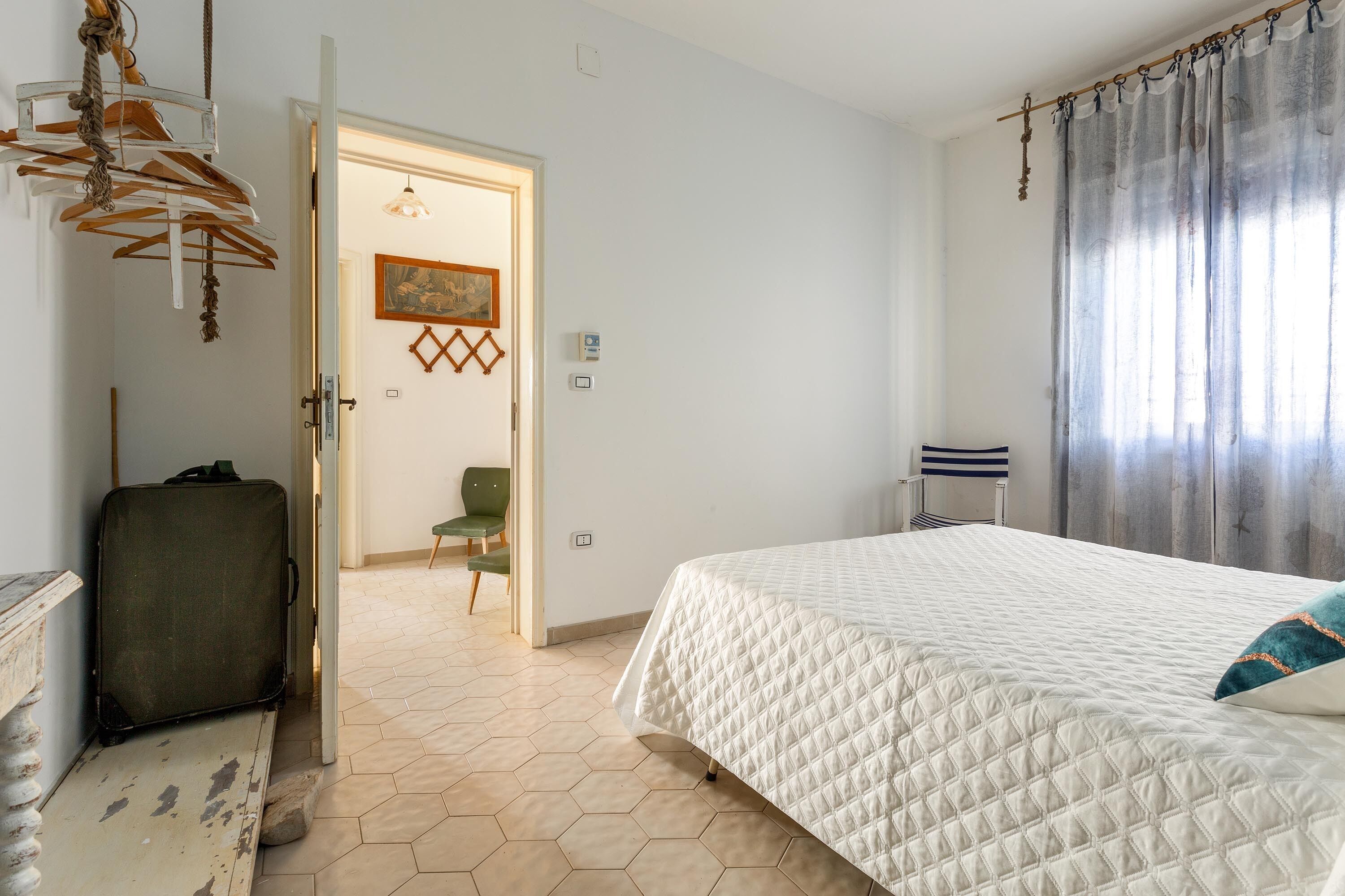 A hotel room with a bed, a suitcase, a chair, and a door leading to another room.