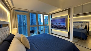 Un dormitorio moderno con una cama grande, un televisor montado en la pared y un balcón con vistas a la ciudad.