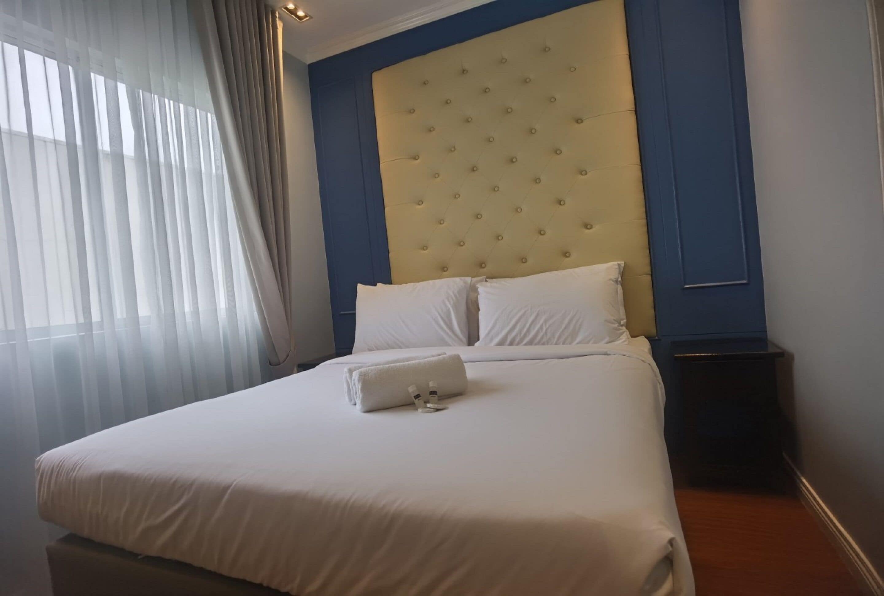 A neatly made bed with white linens and pillows, a tufted headboard, and a bedside table with a lamp.