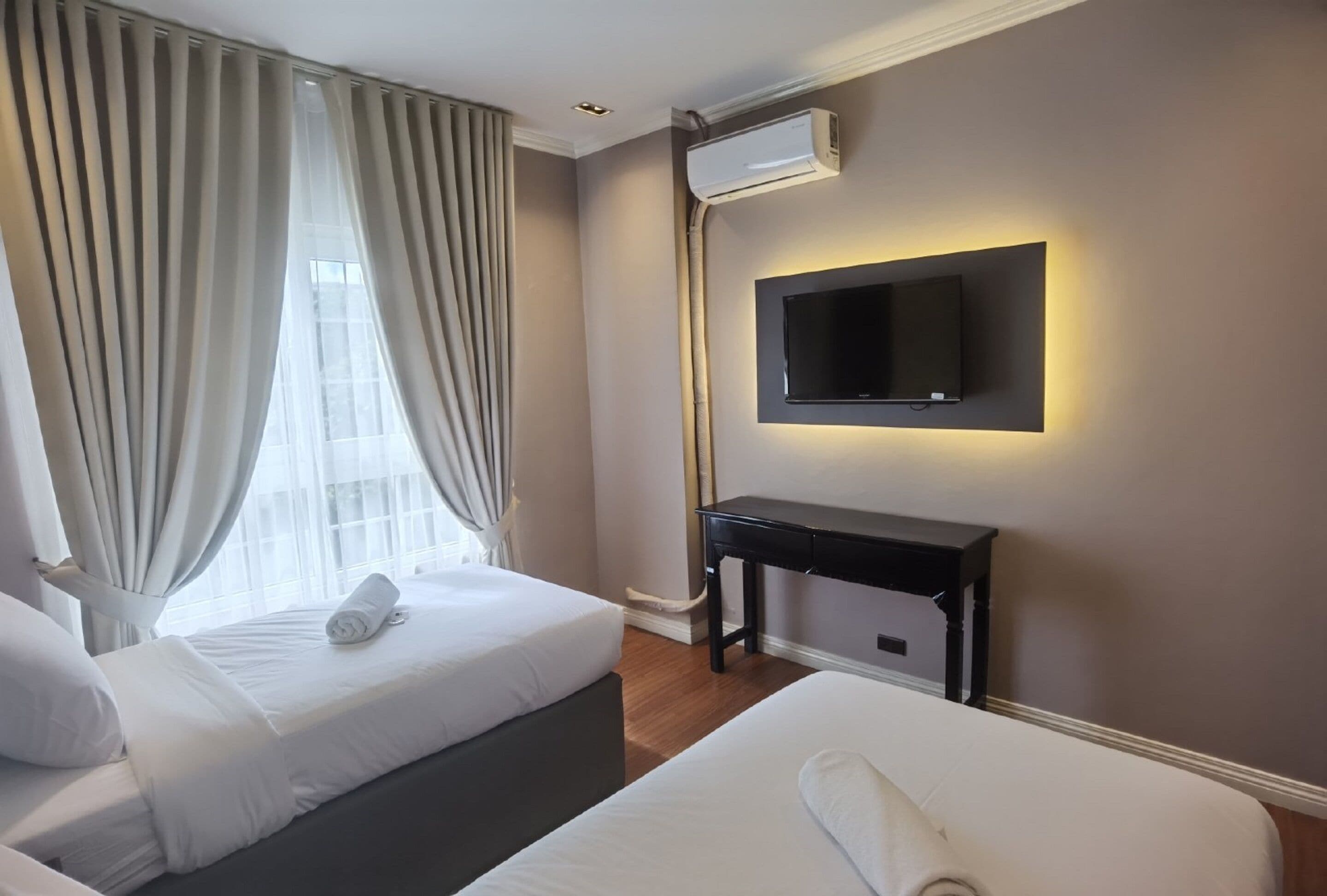 Quarto de hotel com duas camas, uma televisão presa à parede e um ar condicionado.
