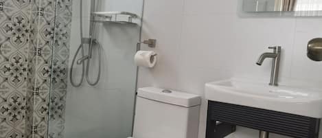 Un baño con inodoro, lavamanos, ducha y zona de ducha con paredes de vidrio.
