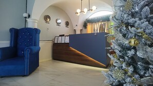 Een receptiegedeelte met een blauwe gestoffeerde fauteuil, een houten receptiebalie en een kerstboom met gouden versieringen.
