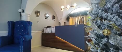 A reception area with a blue upholstered chair, a wooden reception desk, and a Christmas tree with gold ornaments.