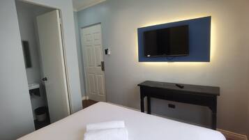 Una habitación de hotel con cama, televisor montado en la pared, un escritorio pequeño y una puerta que da al baño.