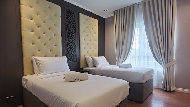 Een hotelkamer met twee bedden, een groot gestoffeerd hoofdeinde, een decoratief paneel en een groot raam met gordijnen.