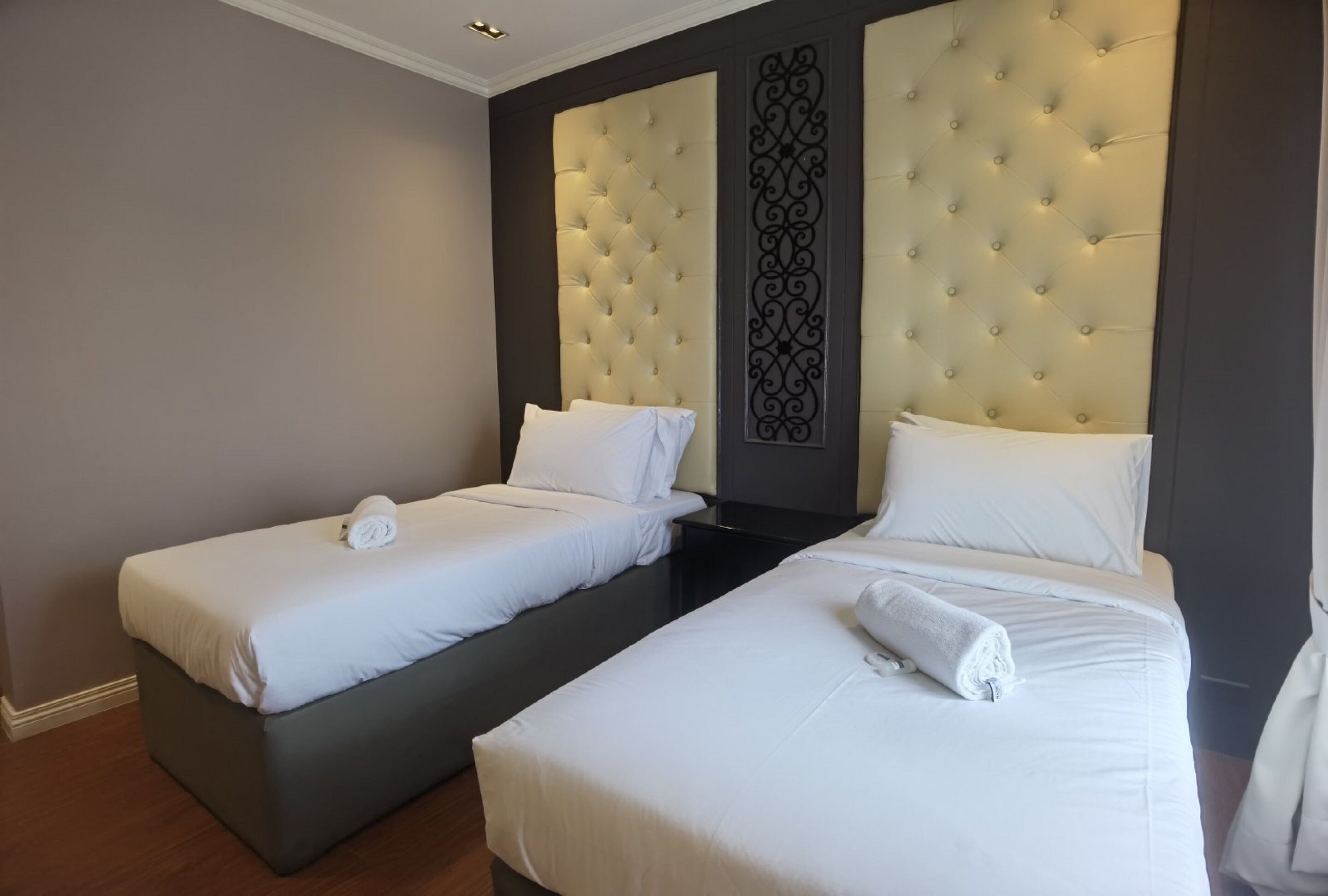 Habitación de hotel con dos camas individuales, cada una con cabecero acolchado y ropa de cama blanca.
