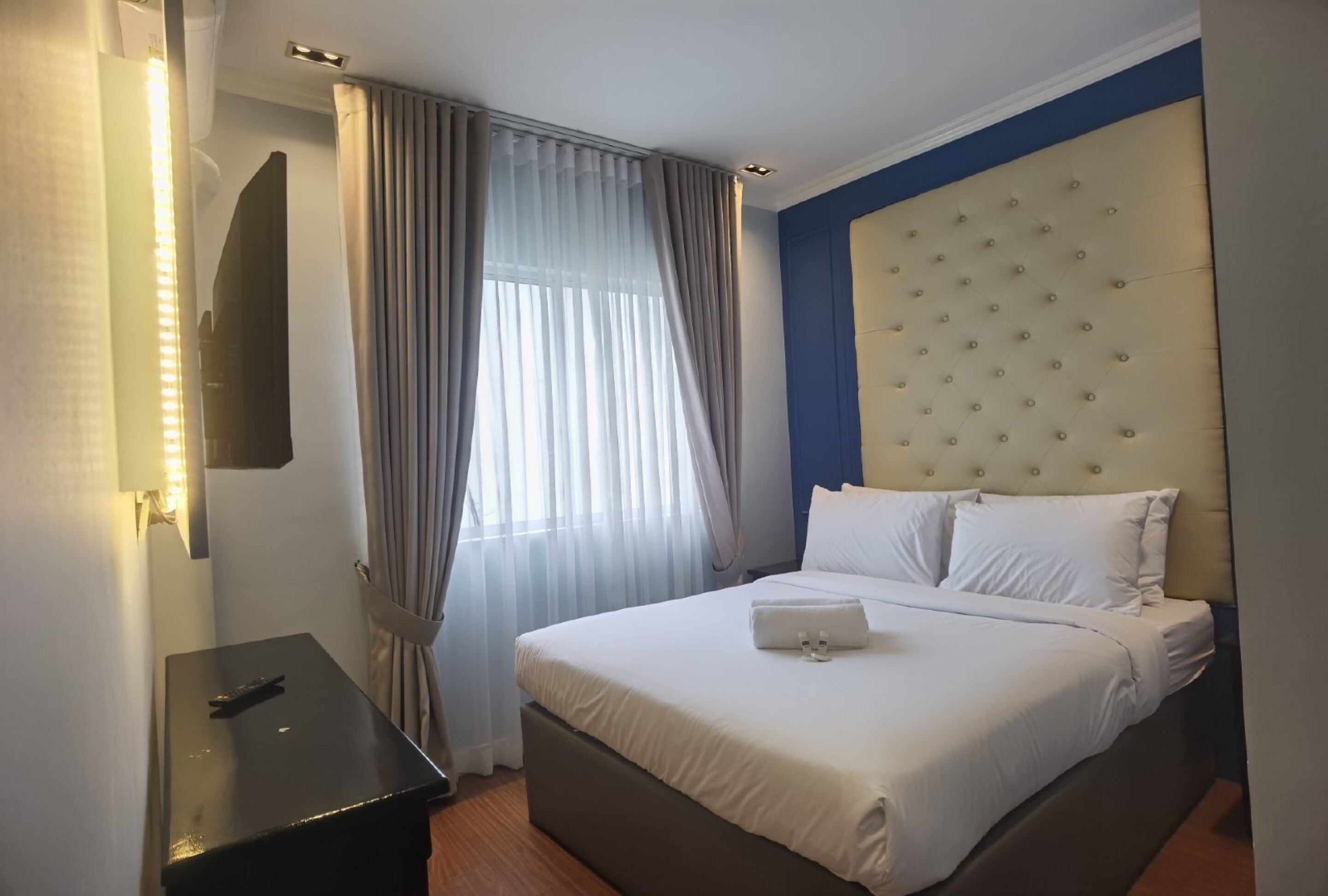 A hotel room with a bed, a bedside table, a mirror, and a window with curtains.