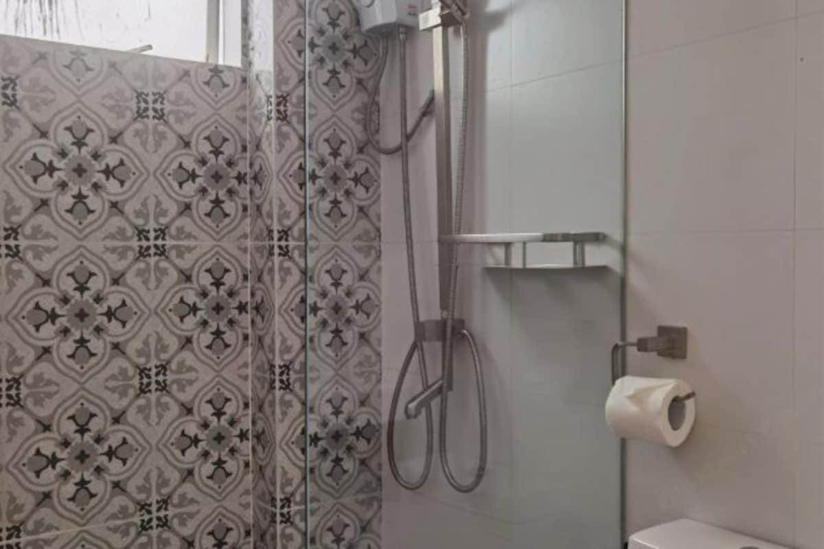 A bathroom with a shower, toilet, and a roll of toilet paper on the wall.