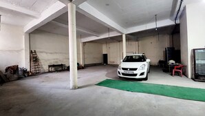 Un'ampia area interna con un'auto bianca parcheggiata vicino a un pilastro, un tappetino verde sul pavimento e un televisore appoggiato al muro.