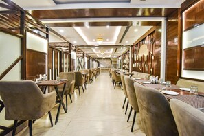 A long dining area with multiple tables and chairs, a chandelier, and wooden paneling on the walls.