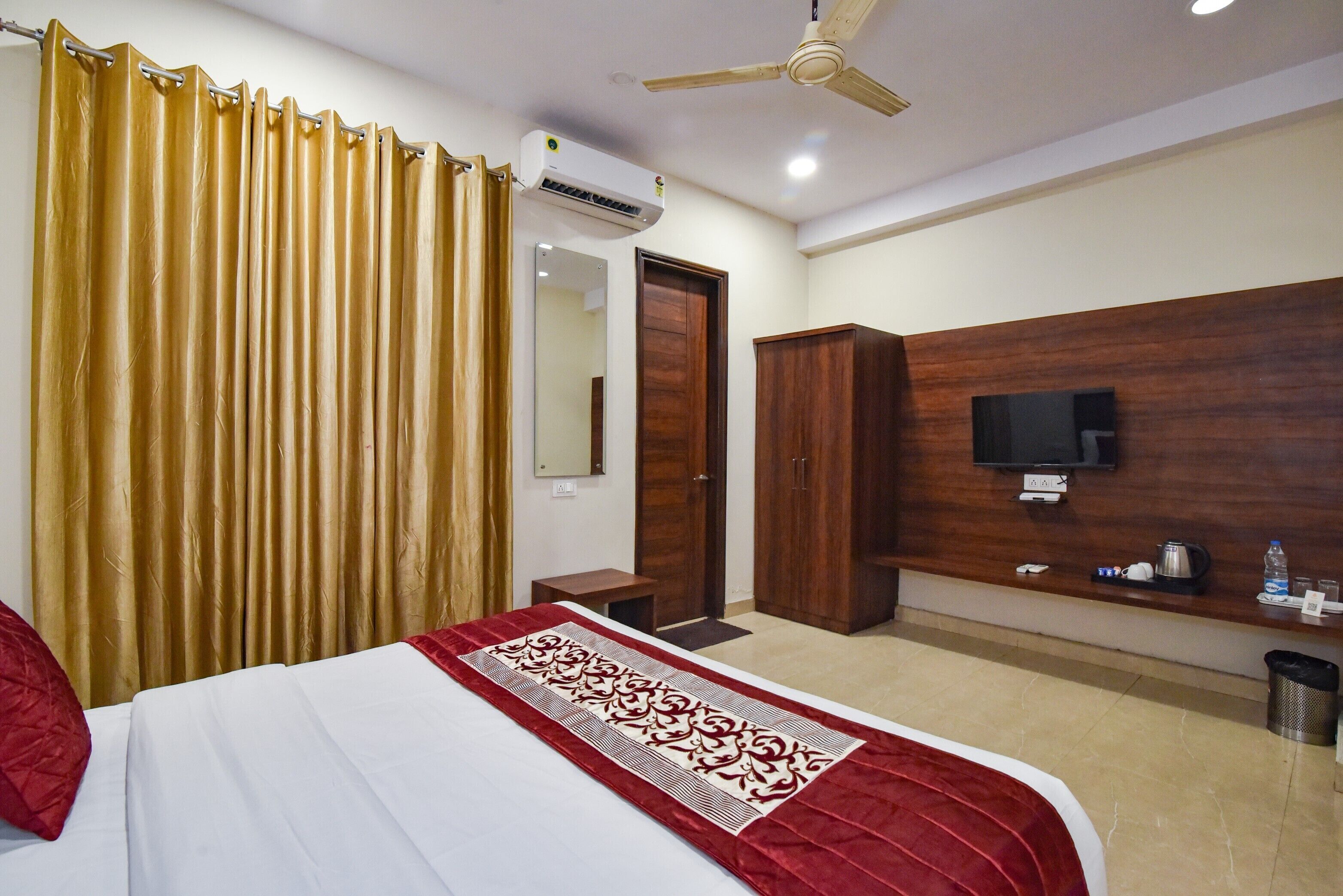 A hotel room with a bed, a television, a wardrobe, a mirror, and an air conditioning unit.