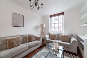 A modern living room with two sofas, a glass coffee table, a lamp, and a large window with blinds.