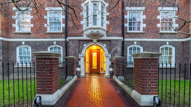 A brick building with a central archway and a red brick pathway leading to it. - 3 Bed Apartment in St John’s Wood (London)