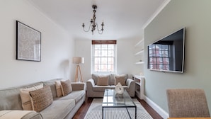 A living room with a sofa, coffee table, and a TV mounted on the wall. - 3 Bed Apartment in St John’s Wood (London)