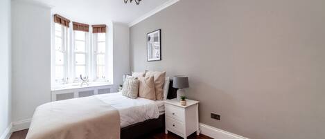 A bedroom with a bed, bedside table, lamp, and a picture on the wall.