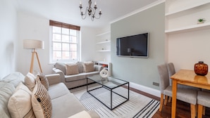 A modern living room with a sofa, coffee table, and TV. - 3 Bed Apartment in St John’s Wood (London)