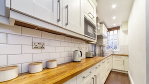 A modern kitchen with white cabinets, a wooden countertop, a built-in oven, and a window providing natural light. - 3 Bed Apartment in St John’s Wood (London)