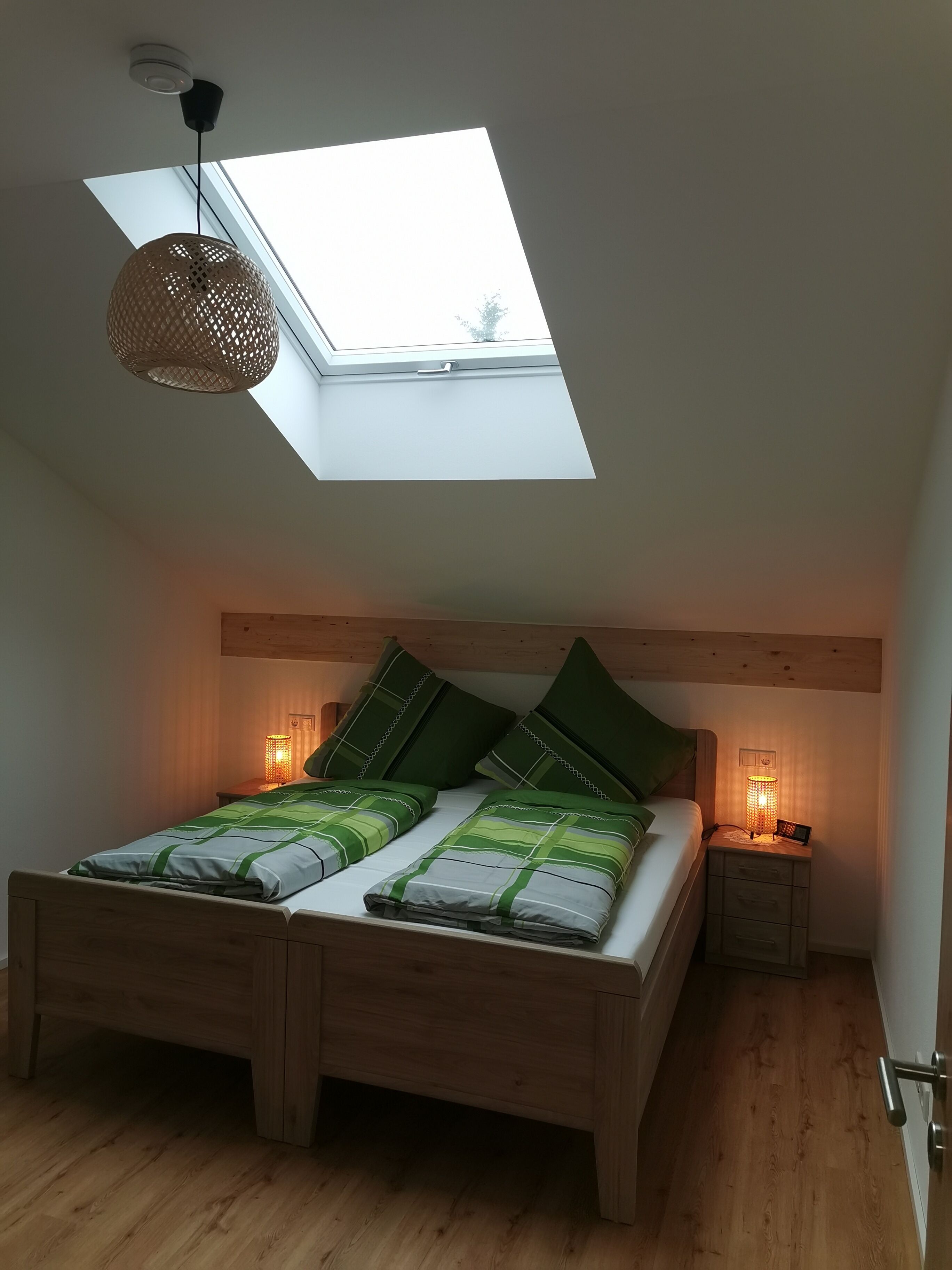 Une chambre à coucher avec un puits de lumière, un cadre de lit en bois, une literie verte et des lampes de chevet.