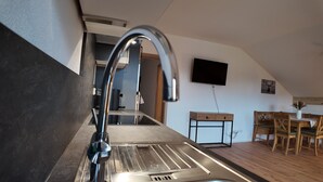 A modern kitchen with a stainless steel sink, a built-in stove, and a wooden dining table with chairs. - Nr. 1 Neubau Ferienwohnung mit 2 Sep. Schlafzimmern, Ost-balkon, 75qm (Prien am Chiemsee)