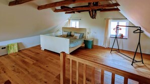 Une chambre avec un plafond en pente, des poutres en bois, un lit, une petite table et une fenêtre.