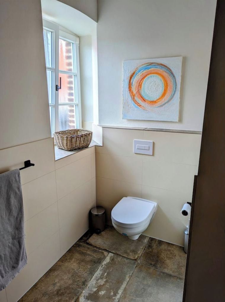 Een kleine badkamer met een toilet, een prullenbak, een raam en een wandmandje.