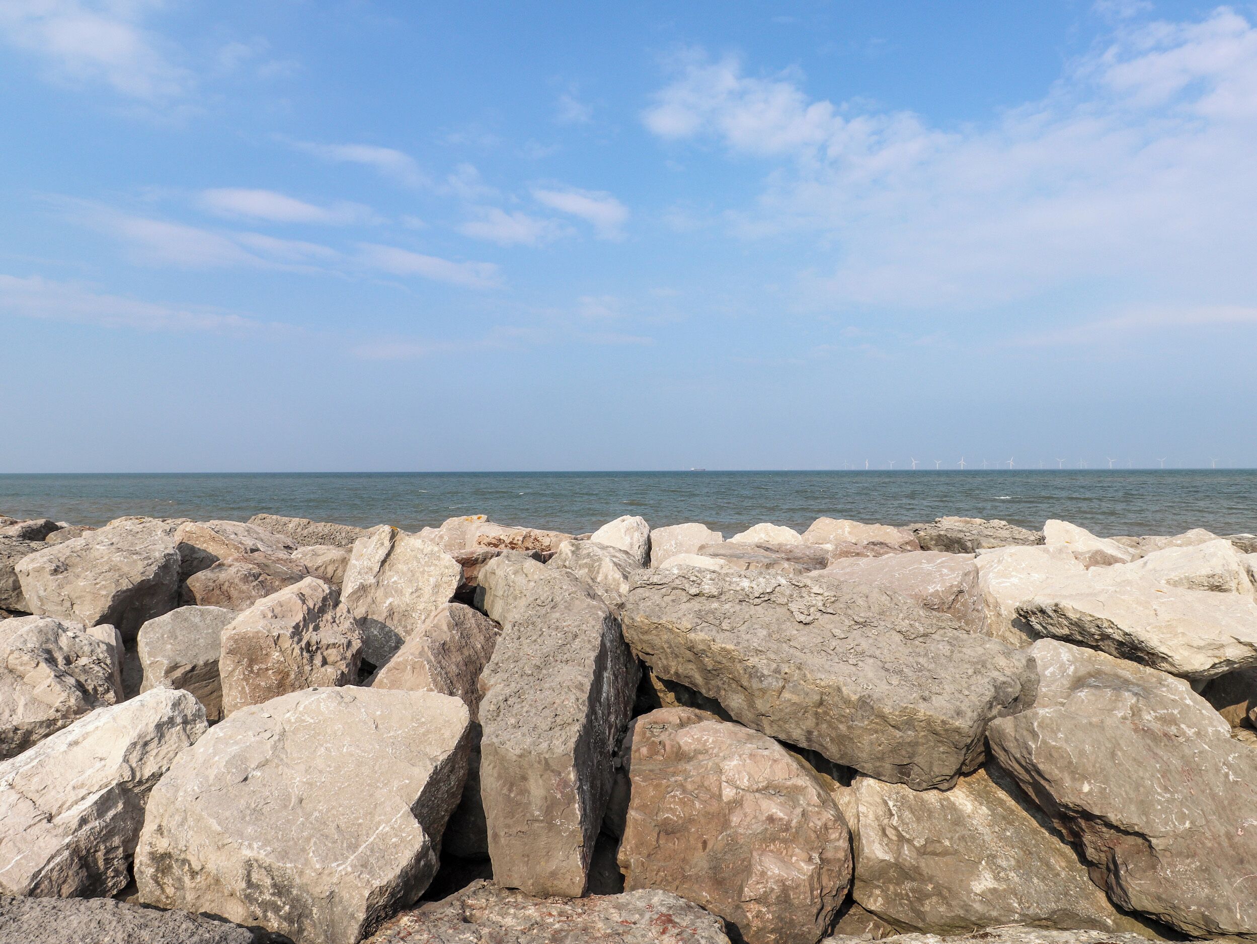 Un rivage rocheux, avec de gros blocs de pierre au premier plan et un ciel dégagé.