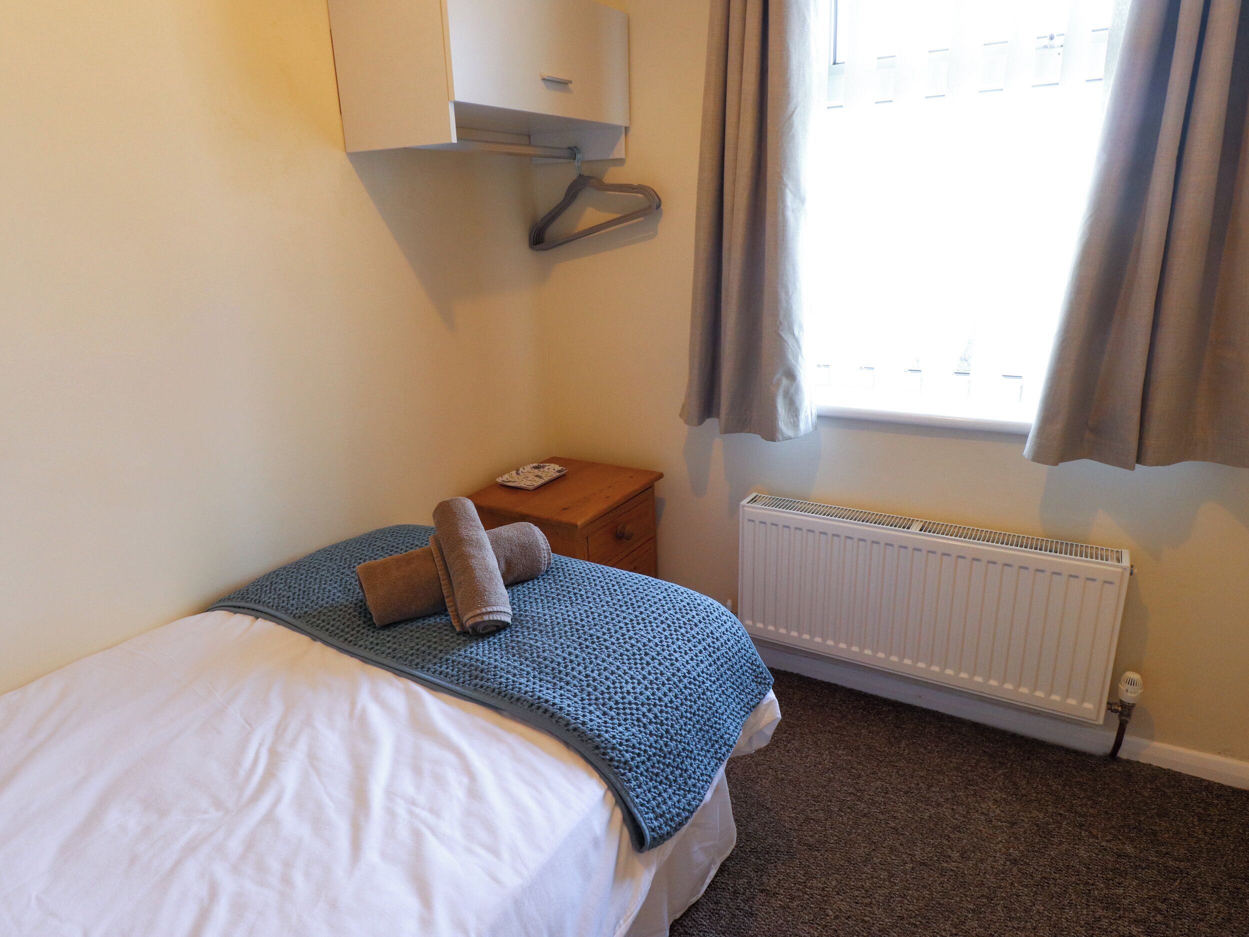 Ein Schlafzimmer mit einem Bett, einem Nachttisch, einem Heizkörper und einem Fenster mit Vorhängen.