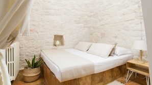 A bedroom with a stone wall, a bed with white linens, a bedside lamp, and a potted plant. - 3676 Villa Enò by Perle di Puglia (Noci)