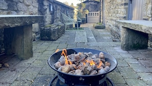 A stone courtyard with a fire pit in the center, surrounded by stone walls and benches.