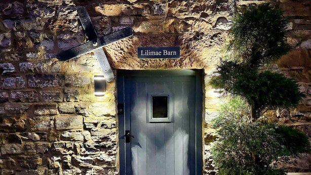 A stone wall entrance with a dark wooden door labeled "Lilimee Barn."